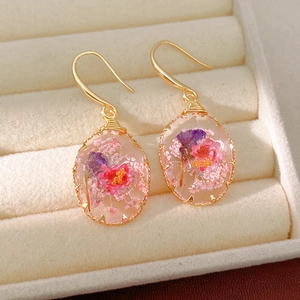 Detailed view of handmade resin earrings with dried pink flowers in a gold setting