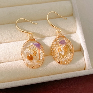 Close-up of teardrop resin earrings with embedded purple and white dried flowers