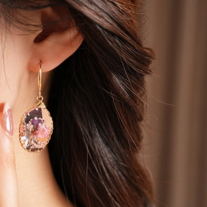 Close-up of elegant oval resin earrings featuring embedded pink and purple dried flowers