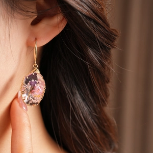 Close-up detail of pastoral style oval resin drop earrings with embedded pink dried flowers