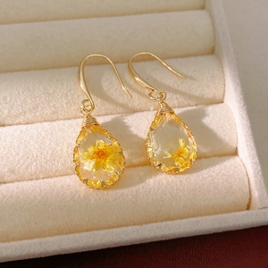 Close-up of elegant gold hook earrings with resin teardrop pendants and dried yellow flowers