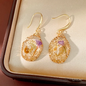 Close-up of oval resin drop earrings with delicate purple and white dried flowers inside
