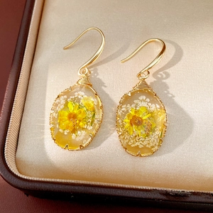 Detailed macro view of oval resin earrings featuring yellow sunflowers and tiny dried flowers
