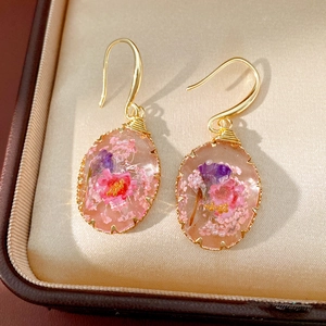 Detail of handmade oval resin earrings featuring real dried pink and purple flowers