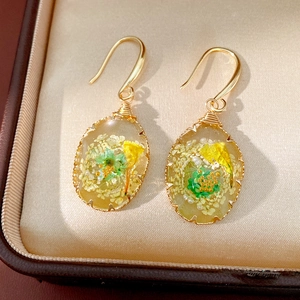 Detail view of oval resin drop earrings with embedded green and yellow dried flowers