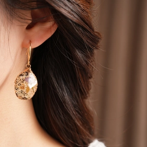 Close-up of pastoral oval resin earrings with embedded dried flowers on a model's ear