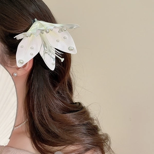Detailansicht einer weißen Lilien-Haarklammer mit Perlenverzierung im Haar des Modells.
