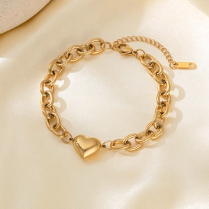 Polished gold heart charm bracelet with thick chain links on beige satin fabric