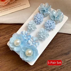 Close-up detail showing a set of five pairs of elegant blue flower earrings with pearls.