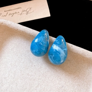Detail showing the macro texture of blue marble teardrop stud earrings on a textured tray