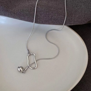 Close-up of a silver snake chain necklace with round ball charm on white ceramic plate