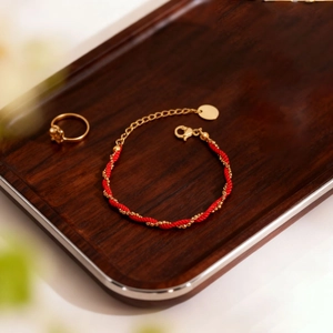 Chinese red cord bracelet and gold flower ring set on an elegant wooden tray