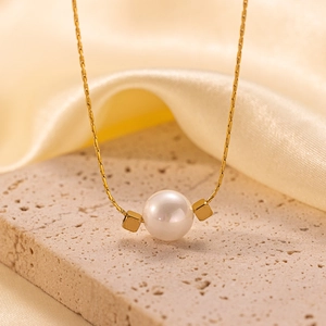 Detail of elegant gold chain necklace with round white pearl and metal accents on stone