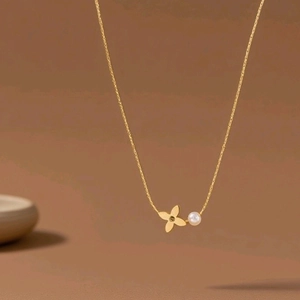 18K gold plated titanium necklace with pearl and four-leaf clover pendant on brown background