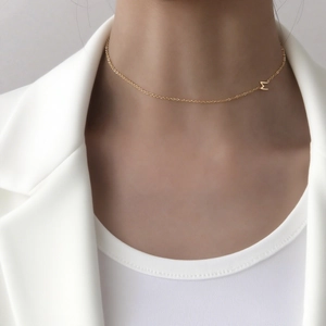 Collier minimaliste en acier titane avec lettre M porté sur un col de costume blanc