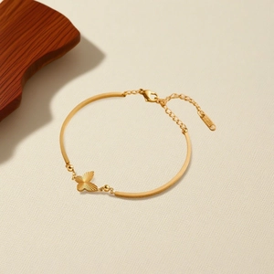 Elegant 18K gold butterfly bracelet with fine chain and textured pendant on cream background