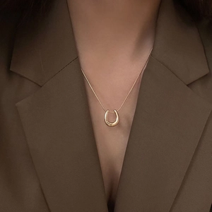 Elegant gold U-shaped pendant necklace shown on model with dark blazer background