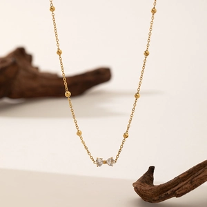 Golden bow bracelet with zircon stones on thin beaded chain over natural wood aesthetic