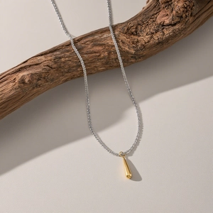 Collana minimalista bicolore con ciondolo a goccia su sfondo in legno rustico