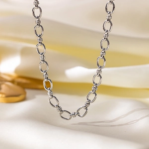 Polished silver Cuban link chain necklace displayed on soft white satin fabric background