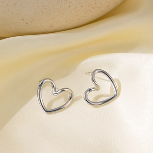 Macro shot of silver hollow heart-shaped stud earrings on a soft satin fabric surface