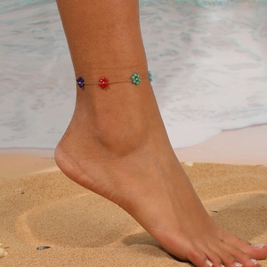 Close-up view of a colorful beaded flower anklet worn on a foot at a summer beach