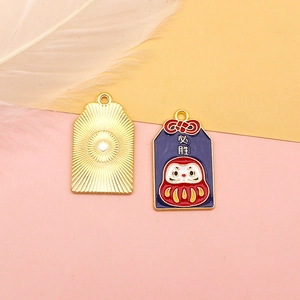 Detail view of Daruma Omamori alloy pendant showing front enamel and gold sunburst back.