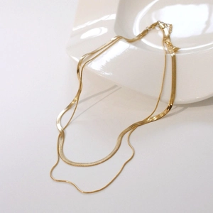 Detail of gold double-layered snake chain necklace on white ceramic display plate