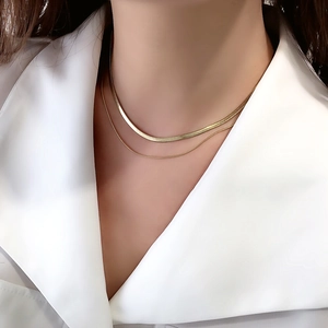 Detail of layered gold snake bone chain necklace on woman wearing a white silk blouse