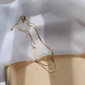 Detail of double-layer gold snake chain necklace featuring a heart pendant on gauze background