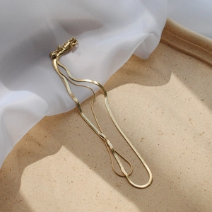 Detail of a double-layered gold snake bone necklace on a textured sand tray with soft lighting