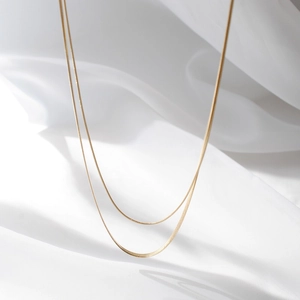 Close-up of golden double-layered snake and box chain necklaces on white silk