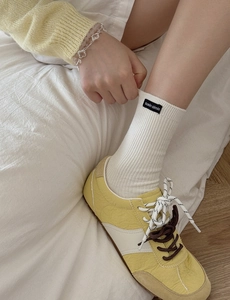 Detail shot of white ribbed mid-calf socks with black cloth label and yellow sneakers