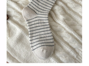 Detailed knit texture of ivory crew socks with dark grey stripes on a soft wool blanket