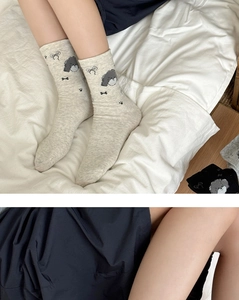 Detail of oatmeal crew socks featuring black bows and cute cartoon dog knit patterns