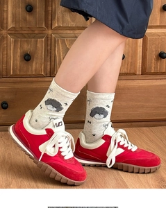 Detail showing red suede sneakers with dog pattern crew socks on a wooden floor
