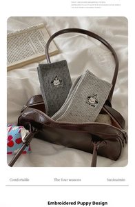 Detail of cute dog embroidery on grey knit crew socks inside a brown leather bag