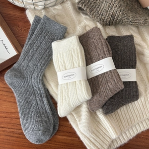 Thick wool knit socks in neutral tones displayed on a cozy white textured background