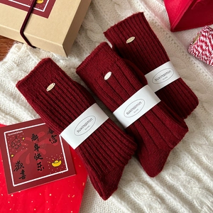 Three pairs of warm red wool socks with ribbed knit and festive gift packaging on white blanket