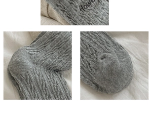 Detail view of grey cable knit socks featuring embroidered flower text and reinforced heel
