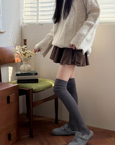 Close-up of dark grey over-the-knee knitted socks with corduroy skirt and cozy sweater
