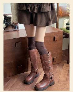Close-up of brown tall biker boots with multi-buckle straps and knit over-knee socks
