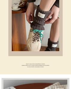 Detail of dark brown cable knit leg warmers with cartoon label and sporty sneakers