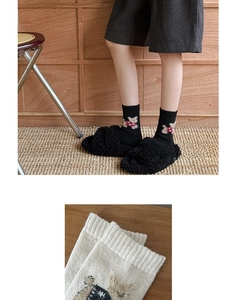 Detail of black wool socks with cute bear pattern and fuzzy slippers on woven rug