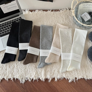 Women's cotton knee-high compression socks in seven neutral colors on a cozy rug