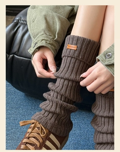 Close-up of brown knitted leg warmers with vintage leather patch and ribbed texture detail