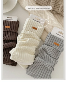 Three pairs of knitted leg warmers in grey and brown with leather labels and packaging