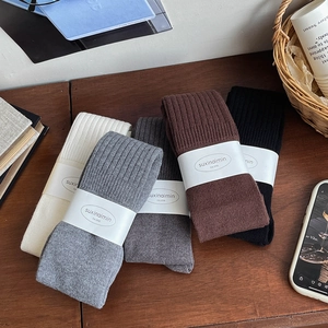 Set of four rib-knit over-the-knee socks in white, grey, brown, and black on wood