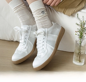 Close-up of white leather sneakers and mesh bow socks on a wooden floor