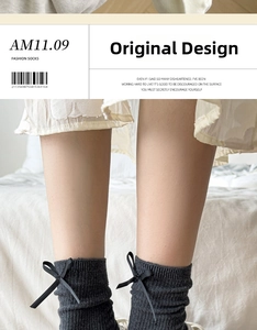 Detail of dark grey ribbed crew socks with a black silk ribbon bow on soft bedding